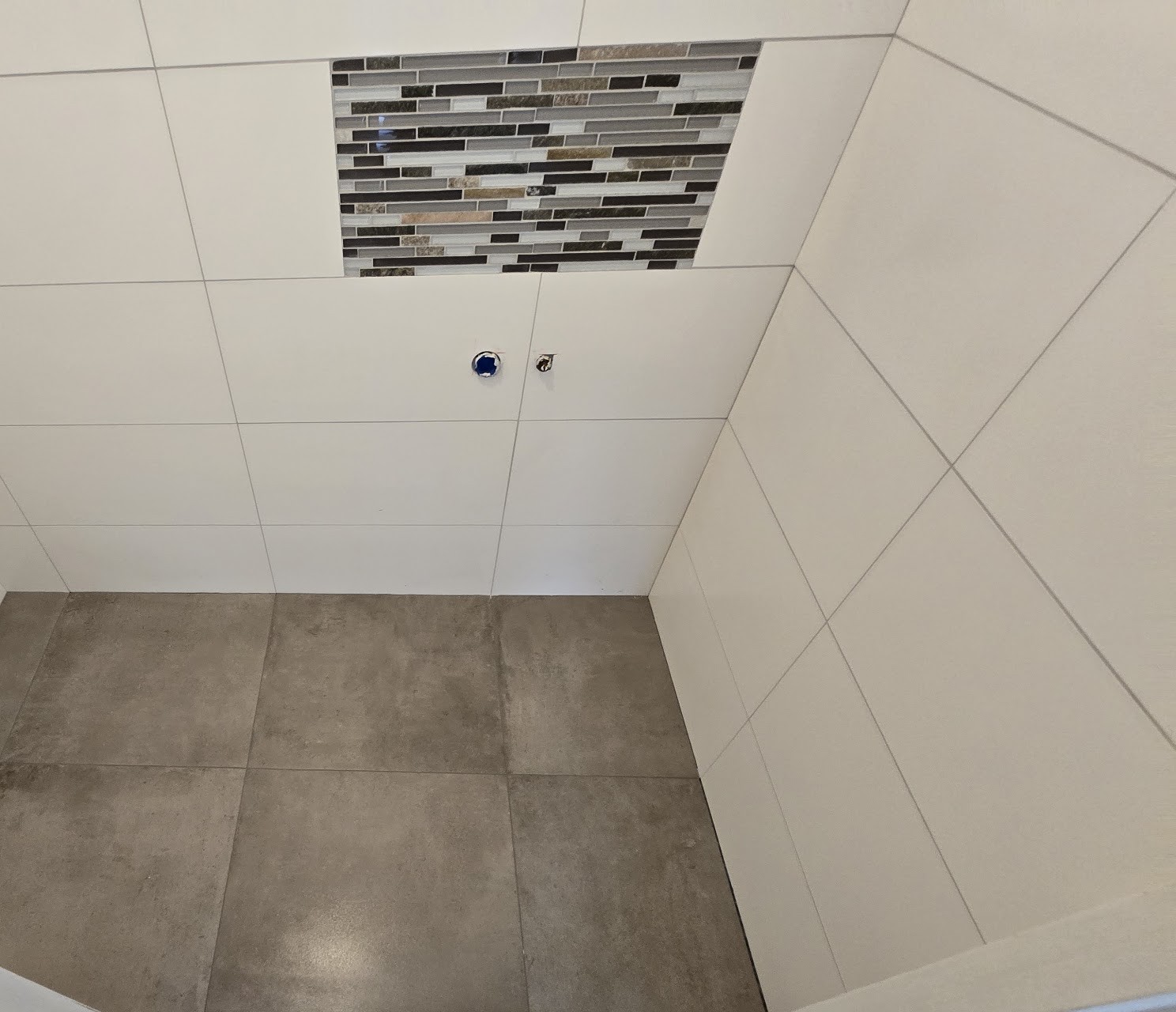 Douche met grijze vloertegels, witte wandtegels en een mozaïekstrook